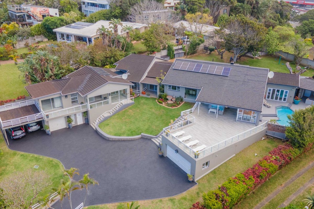 Aerial view of a large residential property featuring a spacious paved driveway, raised deck, swimming pool, and solar panels on a tiled roof.