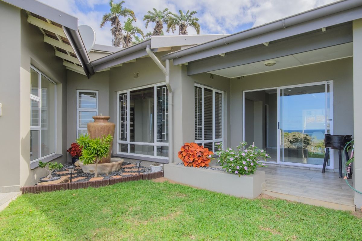 A well-maintained rear exterior featuring a covered patio with tiled flooring, sliding glass doors, and a landscaped garden area with a water feature.