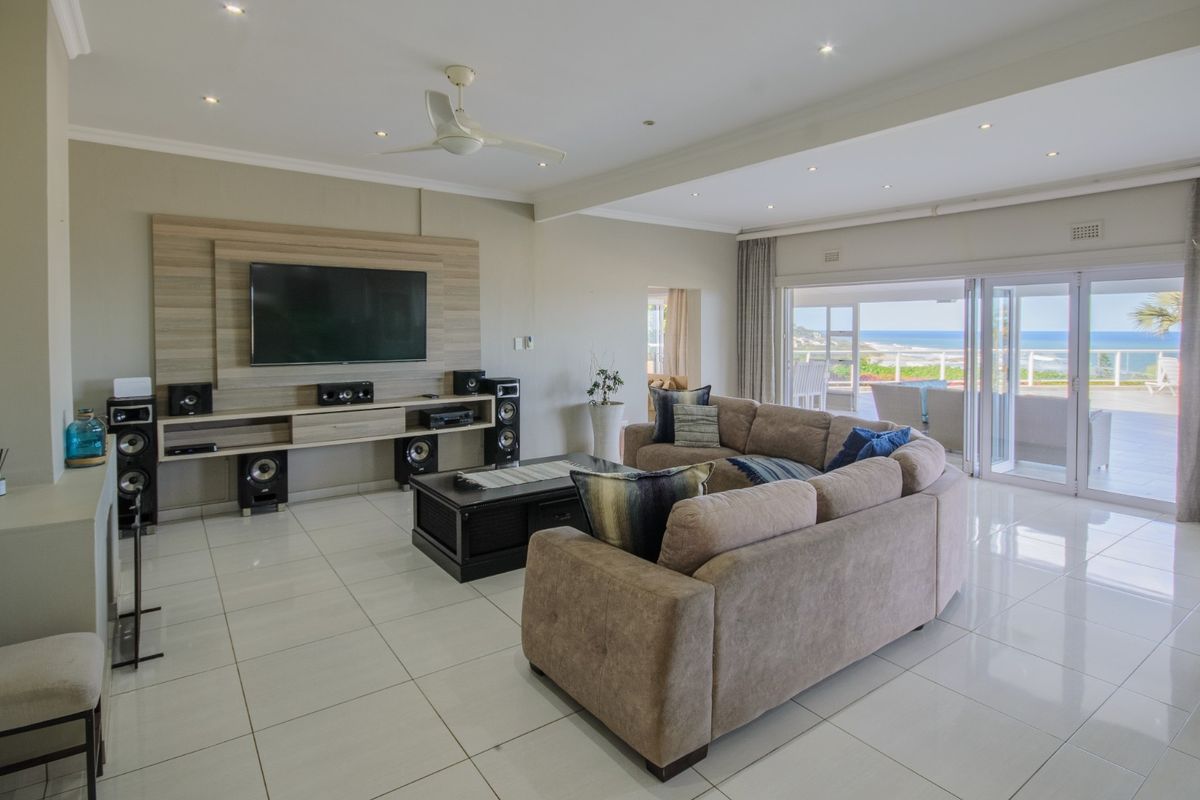 Spacious living room featuring tiled floors, recessed lighting, a built-in media wall, and large sliding doors opening to an outdoor patio with ocean views.