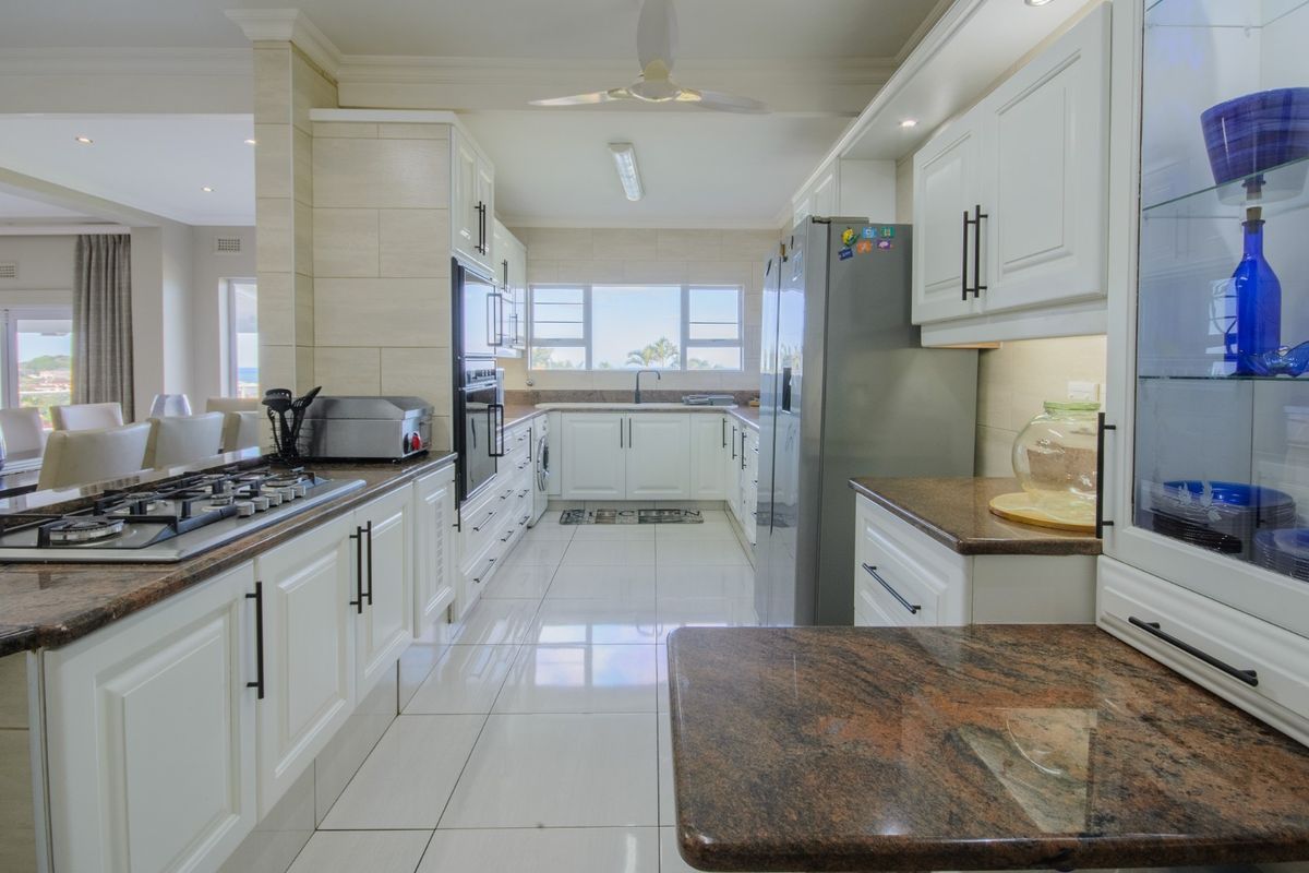 A well-maintained kitchen featuring granite countertops, white cabinetry, built-in oven, gas hob, and tiled flooring, with an open-plan layout connecting to the dining area.