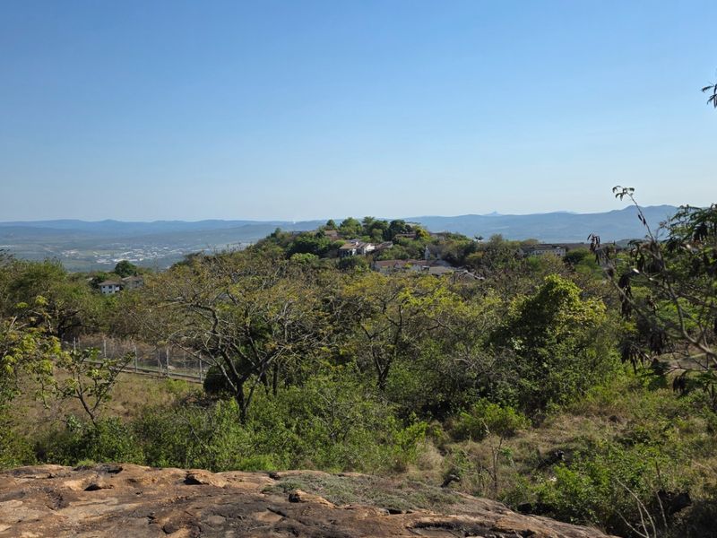 A scenic elevated view overlooking a lush, hilly landscape with distant residential structures and natural vegetation.