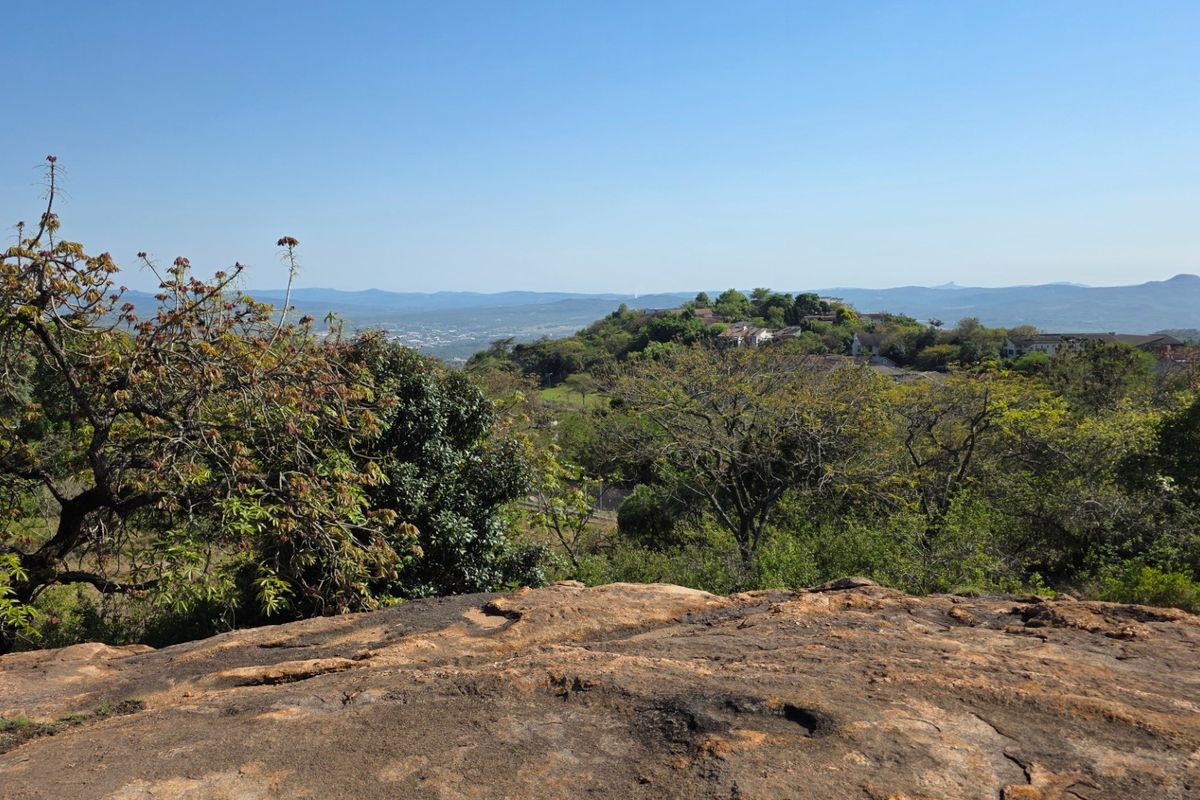 A scenic elevated view overlooking a lush landscape with rolling hills and distant residential areas.