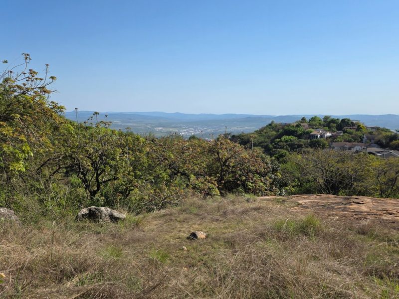 A scenic elevated view overlooking the surrounding landscape, featuring natural rock formations and established indigenous vegetation on the vacant residential land.