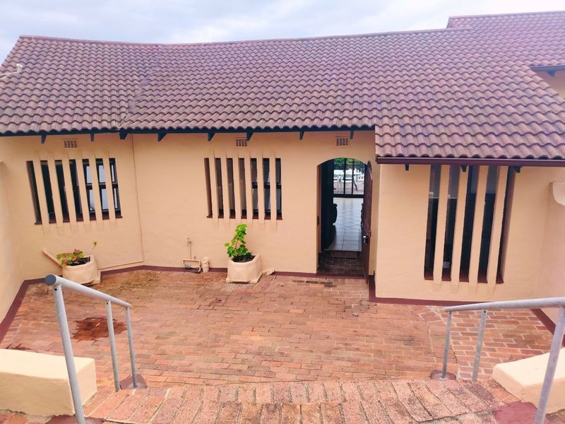 A rear exterior view of the apartment featuring a brick-paved patio area, tiled roof, and secure window bars.