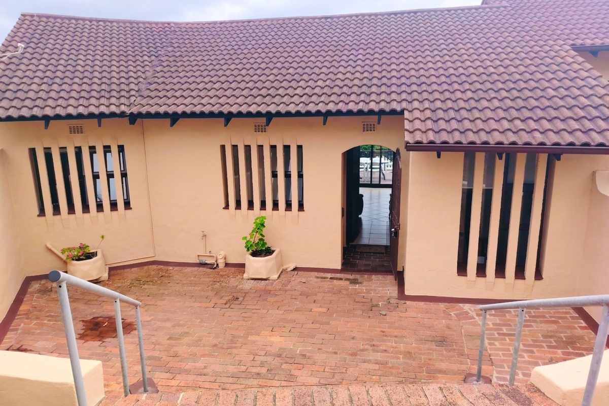 A rear exterior view of the apartment featuring a brick-paved patio area, tiled roof, and secure window bars.