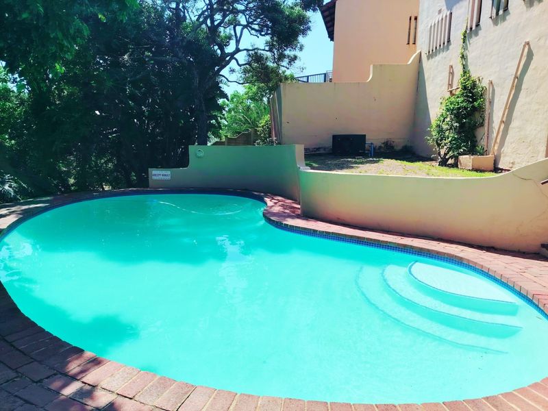A private swimming pool area featuring a curved design, brick coping, and integrated steps, set against a retaining wall and landscaped garden backdrop.