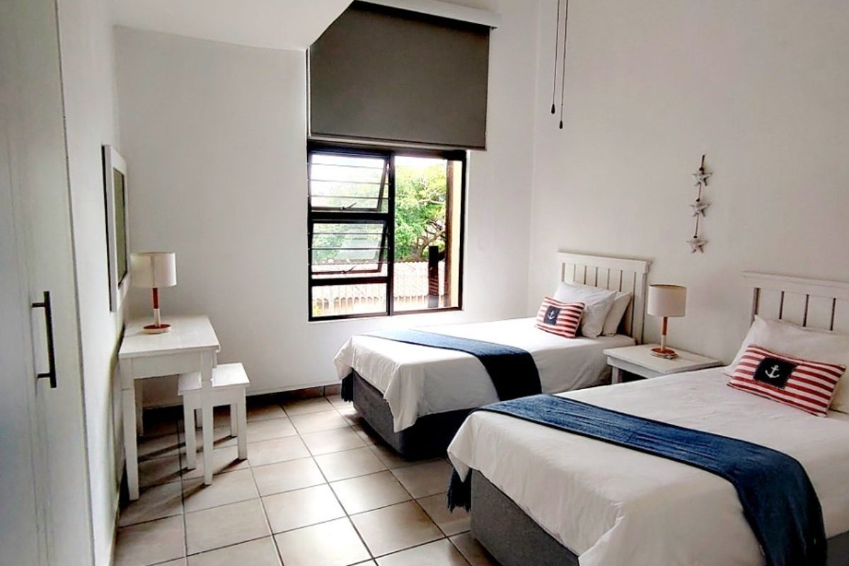 A bright bedroom featuring tiled flooring, a built-in wardrobe, a ceiling fan, and a large window with a roller blind.
