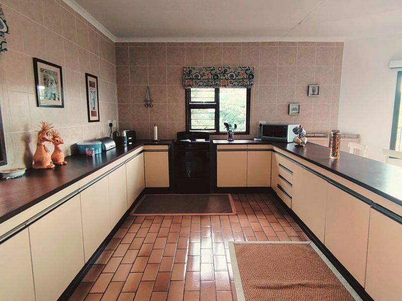 A spacious U-shaped kitchen featuring dated cabinetry, laminate countertops, tiled backsplash, and terracotta floor tiles with a built-in oven.