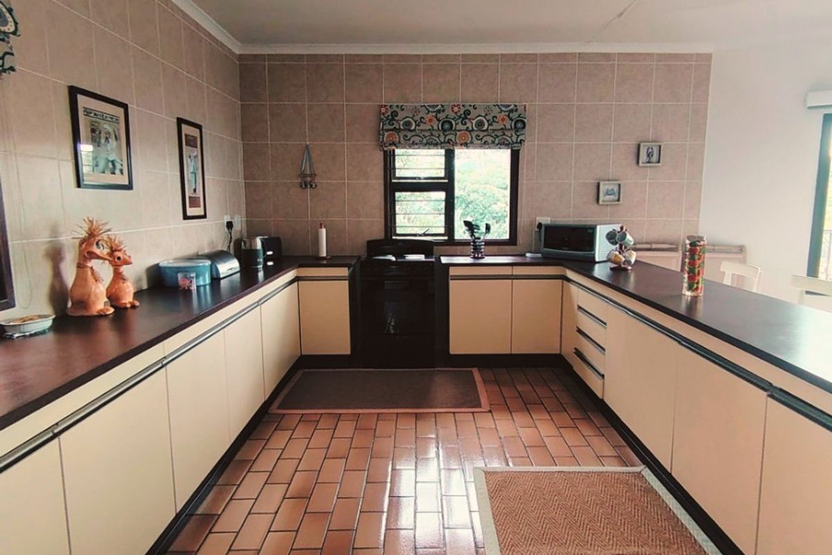 A spacious U-shaped kitchen featuring dated cabinetry, laminate countertops, tiled backsplash, and terracotta floor tiles with a built-in oven.
