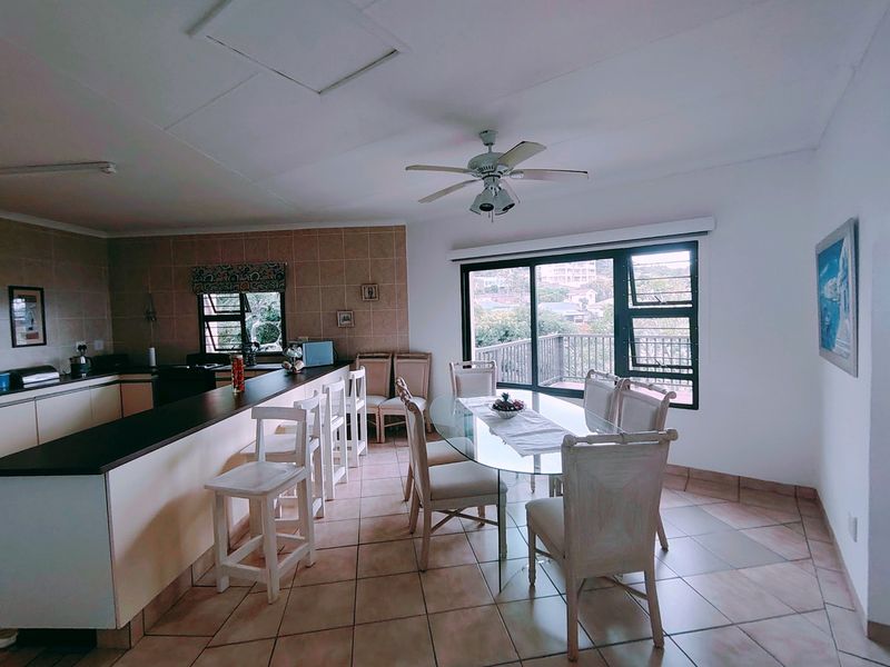 Open-plan kitchen and dining area featuring tiled flooring, a breakfast bar, and large sliding doors leading to an outdoor balcony.