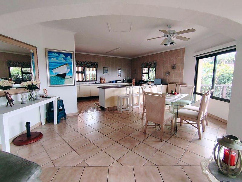 Spacious open-plan living and dining area featuring tiled flooring, a ceiling fan, and a functional kitchen with a central island.