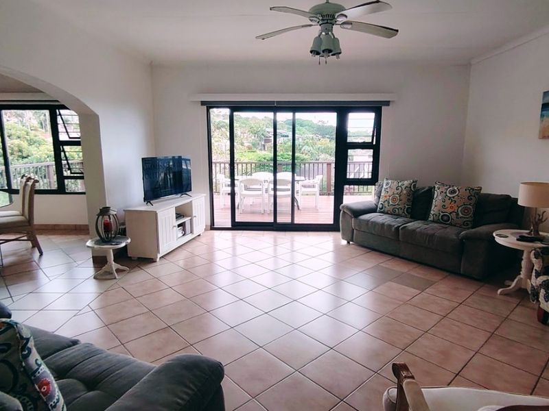 Spacious living room featuring neutral tiled flooring, a ceiling fan, and large sliding glass doors providing access to an outdoor balcony area.