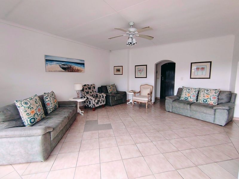 Spacious living room featuring neutral tiled flooring, a ceiling fan, and an arched doorway leading to another area of the apartment.