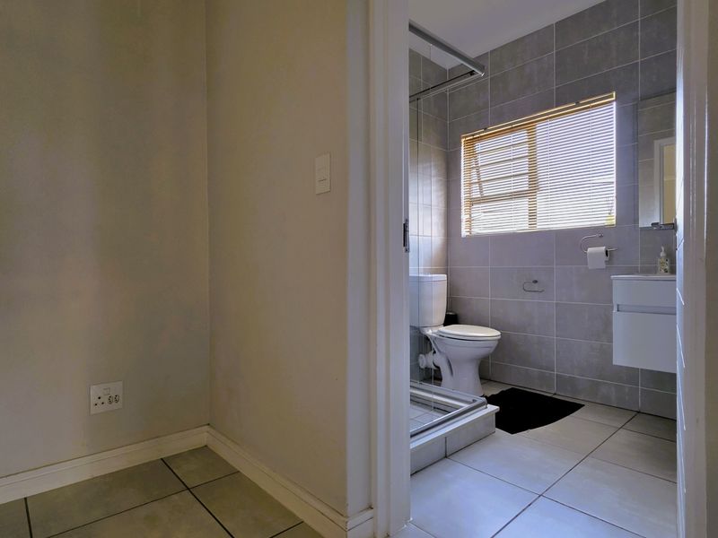A modern bathroom featuring a glass-enclosed shower, a wall-mounted vanity, and neutral grey floor-to-ceiling tiling with natural light from a window.