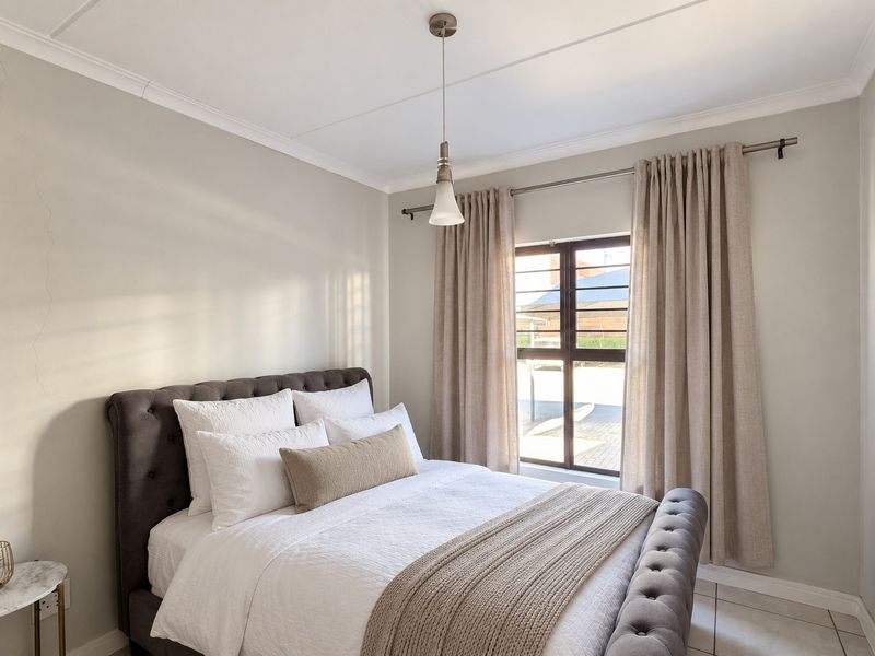 A well-lit bedroom featuring tiled flooring, a central pendant light, and a window fitted with security bars.