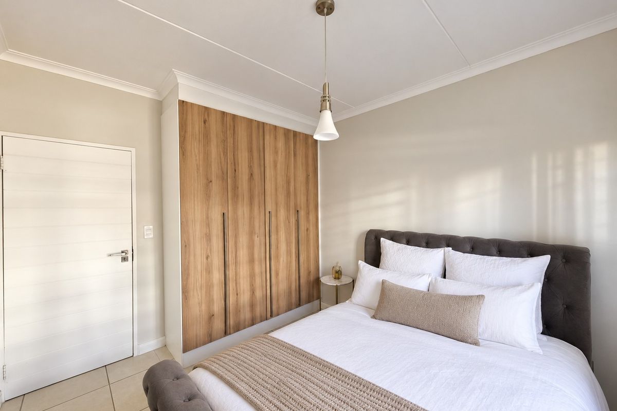 A well-maintained bedroom featuring modern wood-finish built-in cupboards, neutral tiled flooring, and elegant coved ceiling details.