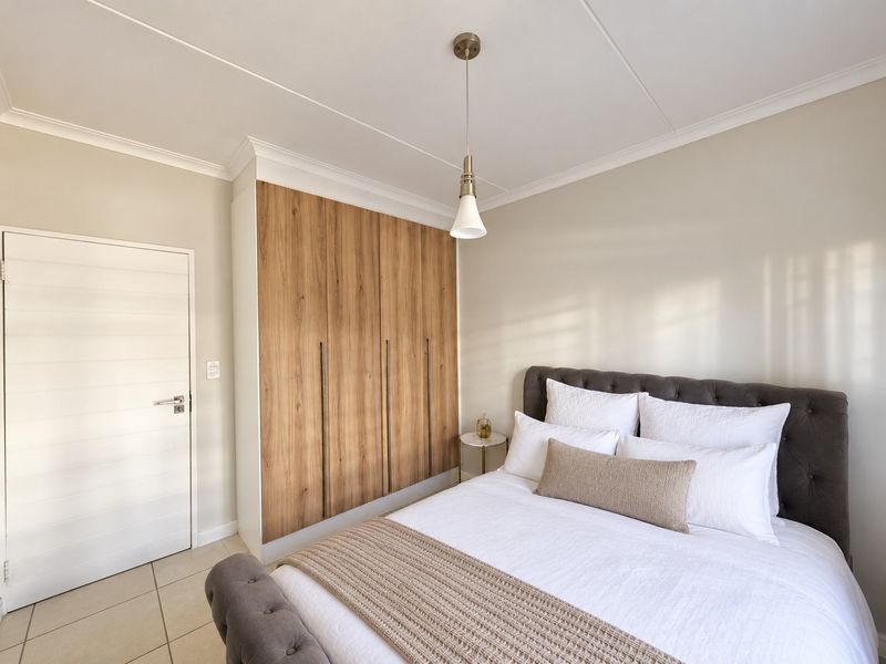 A well-maintained bedroom featuring modern wood-finish built-in cupboards, neutral tiled flooring, and elegant coved ceiling details.