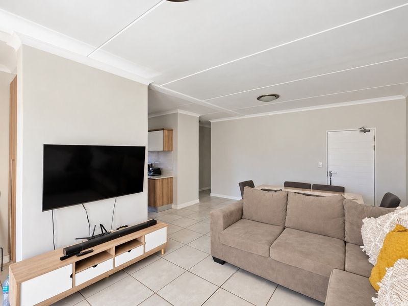 Spacious open-plan living and dining area featuring neutral wall tones, tiled flooring, and a coved ceiling, providing a versatile layout for modern apartment living.
