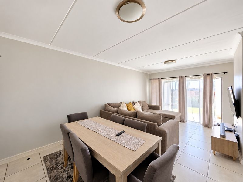 An open-plan living and dining area featuring neutral tiled flooring, coved ceilings, and a large sliding glass door providing access to the exterior.