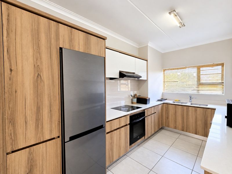Modern kitchen featuring wood-grain cabinetry, stone countertops, integrated appliances, tiled flooring, and a tiled backsplash with ample natural light.
