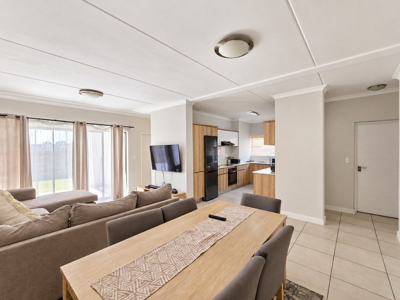 Spacious open-plan living and dining area featuring tiled floors, modern kitchen cabinetry with built-in appliances, and sliding doors leading to an outdoor space.