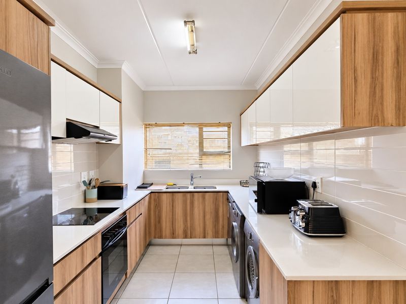Modern galley-style kitchen featuring wood-grain cabinetry, white quartz countertops, subway tile backsplash, integrated appliances, and tiled flooring.
