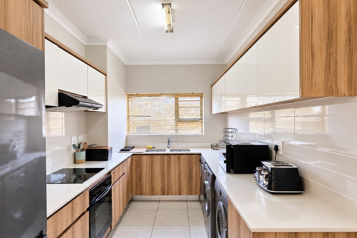 Modern galley-style kitchen featuring wood-grain cabinetry, white quartz countertops, subway tile backsplash, integrated appliances, and tiled flooring.
