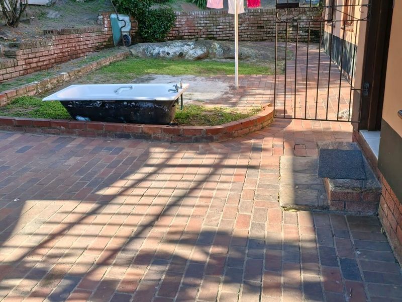 Rear courtyard area featuring brick paving, a retaining wall, and a covered patio section, offering potential for outdoor landscaping and improvement.