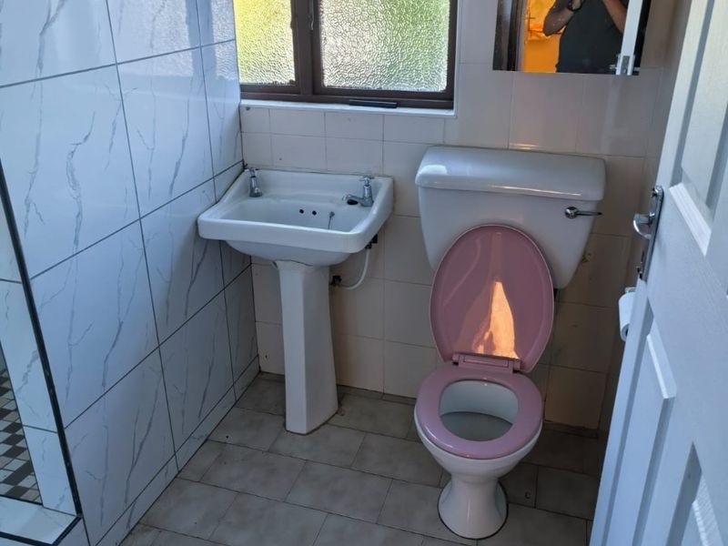 A compact bathroom featuring a pedestal basin, toilet, and tiled finishes, requiring cosmetic updates to modernize the space.