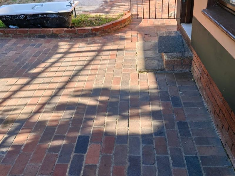 Rear exterior area featuring brick paving, a small brick retaining wall, and a metal security gate leading to the cottage entrance.