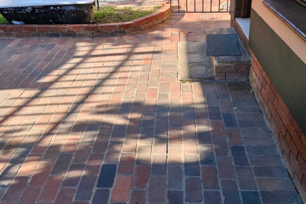 Rear exterior area featuring brick paving, a small brick retaining wall, and a metal security gate leading to the cottage entrance.