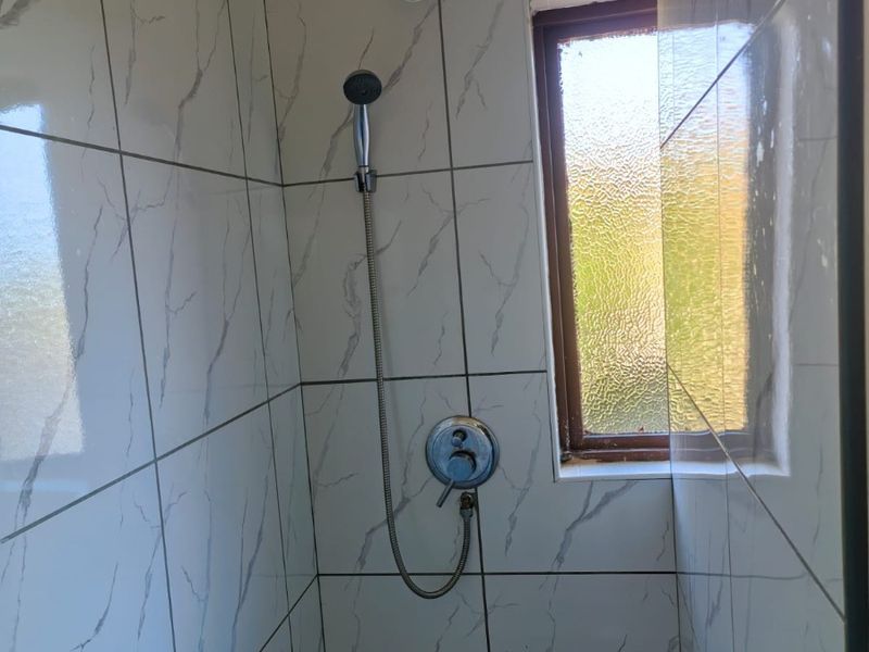 A functional shower enclosure featuring marble-effect wall tiles, a handheld shower mixer, and an obscured glass window for privacy.