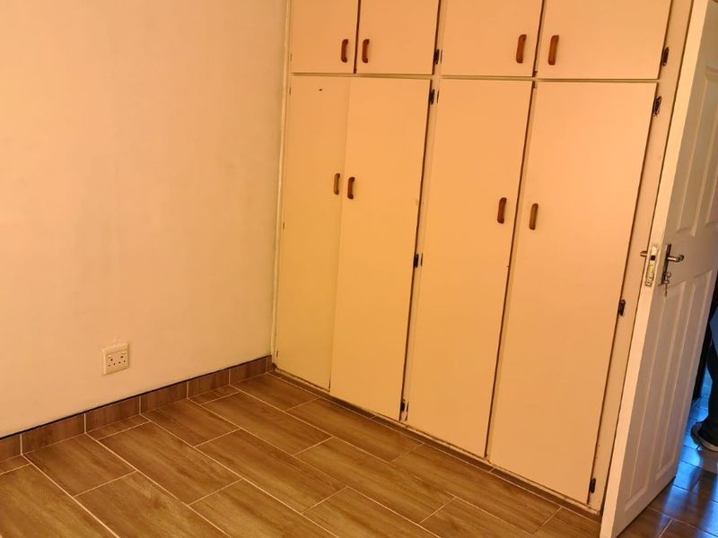 A clean, empty bedroom featuring modern wood-look floor tiles and ample built-in cupboard storage space.