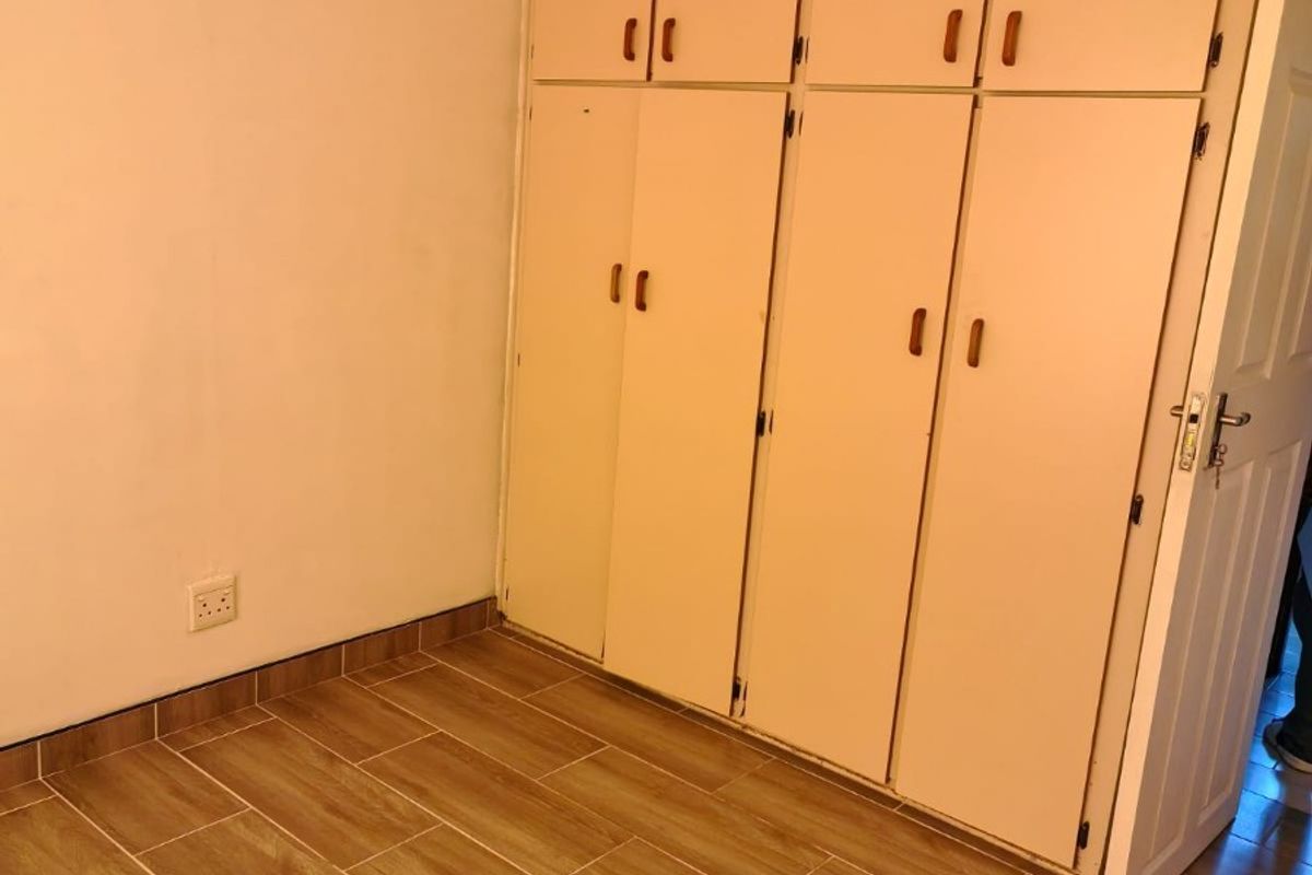 A clean, empty bedroom featuring modern wood-look floor tiles and ample built-in cupboard storage space.