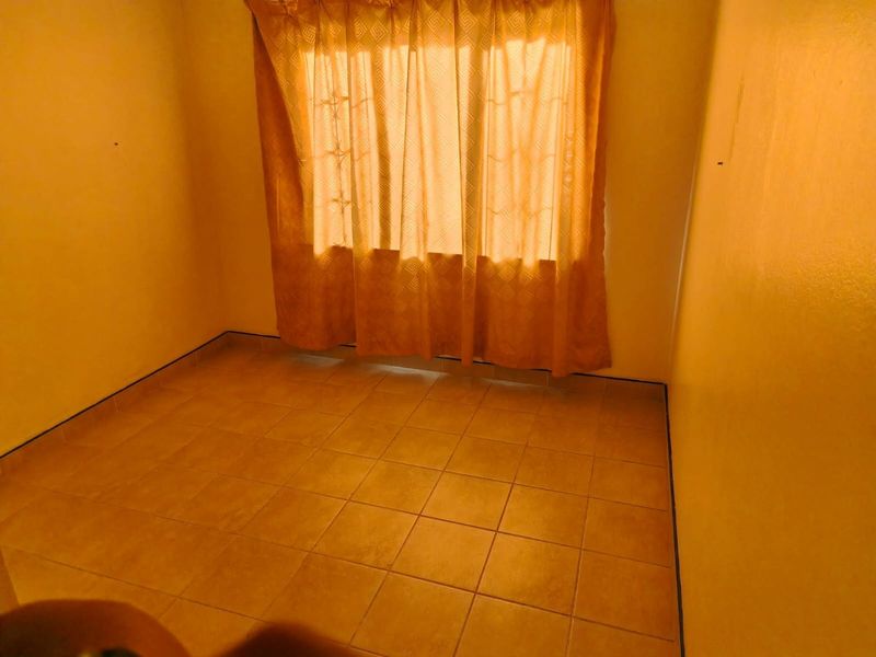 A simple, empty bedroom featuring tiled flooring and a window with security bars, offering a blank canvas for personalization.