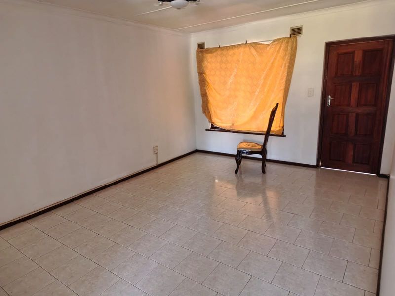 A vacant living room featuring tiled flooring, a timber entrance door, and a ceiling fan, offering a blank canvas for renovation.