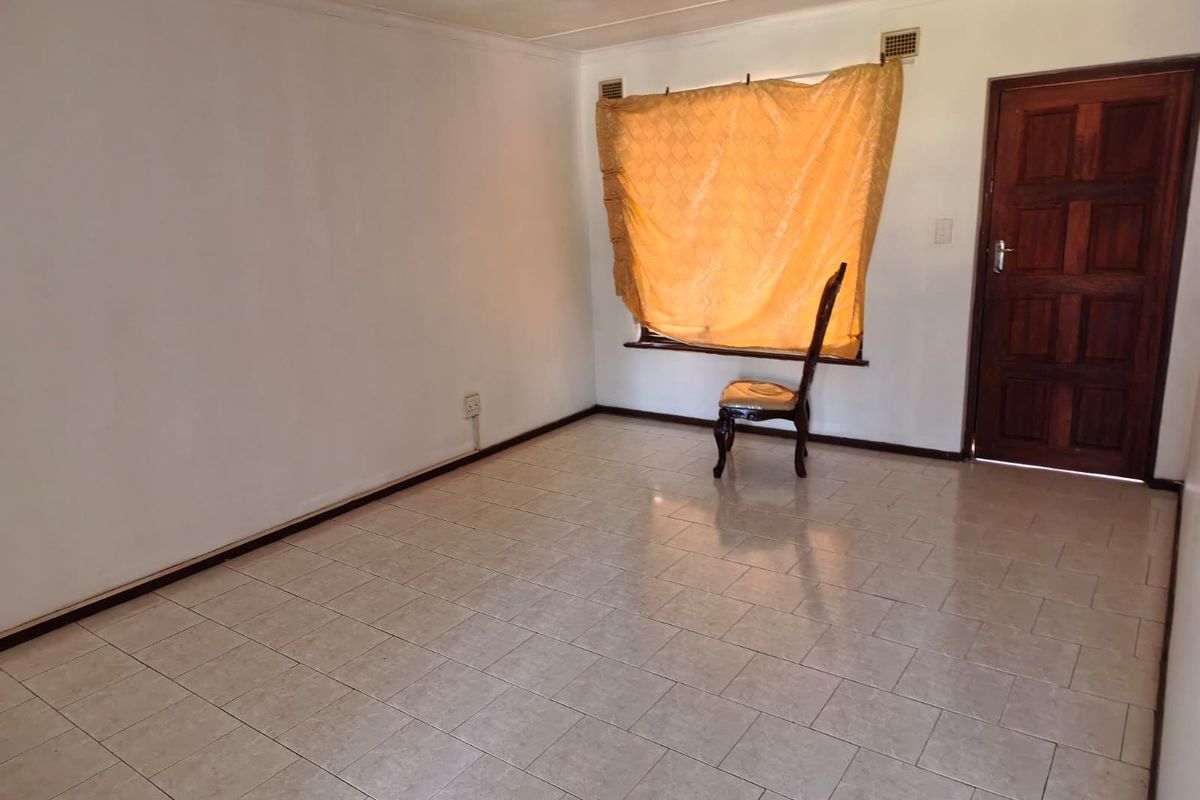 A vacant living room featuring tiled flooring, a timber entrance door, and a ceiling fan, offering a blank canvas for renovation.