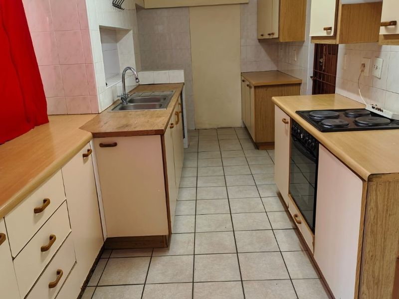 A functional galley-style kitchen featuring laminate countertops, built-in cabinetry, an integrated electric hob and oven, and tiled flooring throughout.