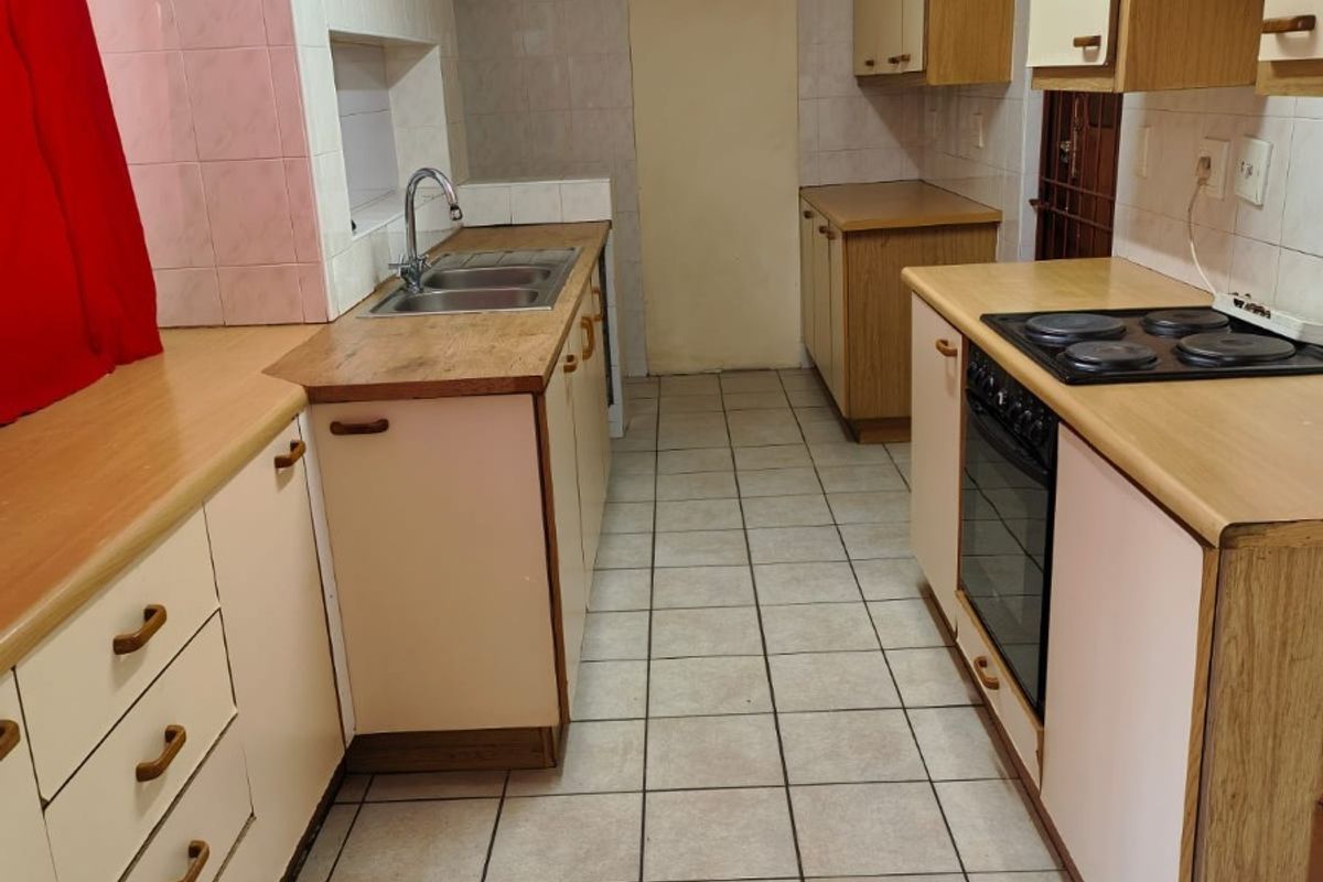 A functional galley-style kitchen featuring laminate countertops, built-in cabinetry, an integrated electric hob and oven, and tiled flooring throughout.