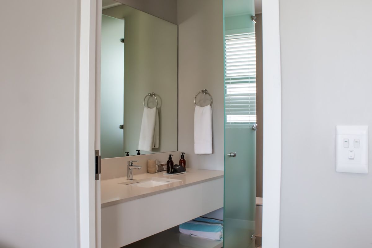 A modern bathroom featuring a sleek vanity with a basin, mixer tap, large wall mirror, and a frosted glass door.