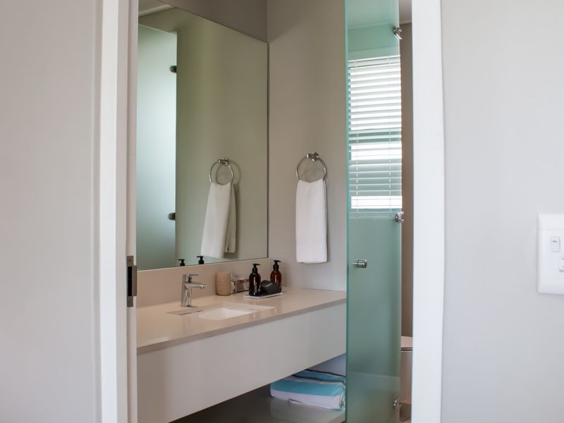 A modern bathroom featuring a sleek vanity with a basin, mixer tap, large wall mirror, and a frosted glass door.
