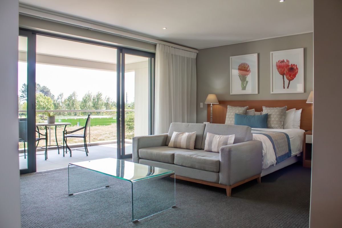 Spacious bedroom featuring a built-in headboard, neutral carpeting, and large sliding glass doors opening onto a private balcony with outdoor seating.