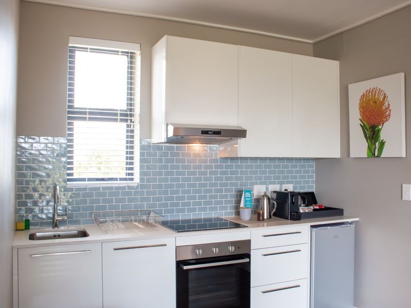 A modern, compact kitchen featuring white cabinetry, a blue subway tile backsplash, built-in oven, electric hob, and a stainless steel sink.