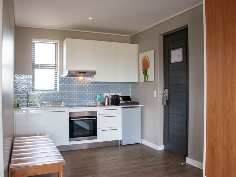 A modern, compact kitchen featuring white cabinetry, a blue subway tile backsplash, integrated oven and hob, and durable laminate flooring.