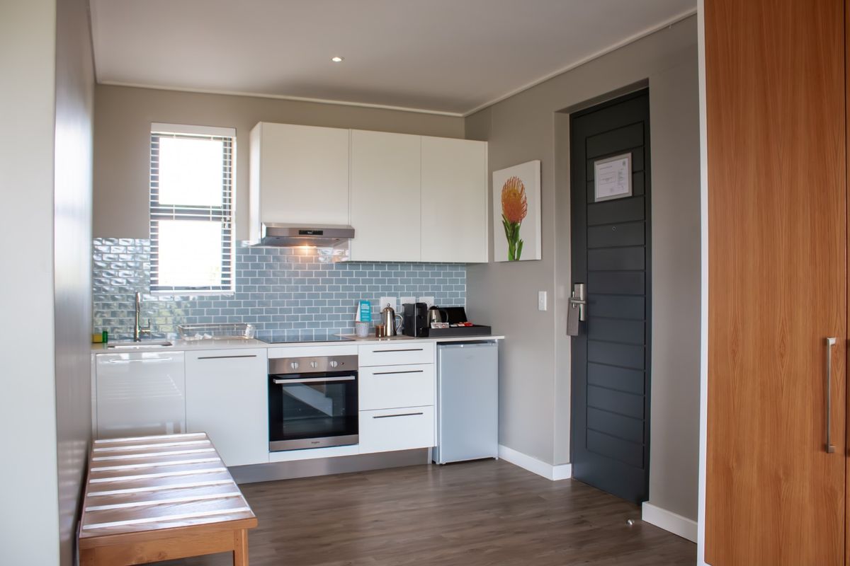 A modern, compact kitchen featuring white cabinetry, a blue subway tile backsplash, integrated oven and hob, and durable laminate flooring.