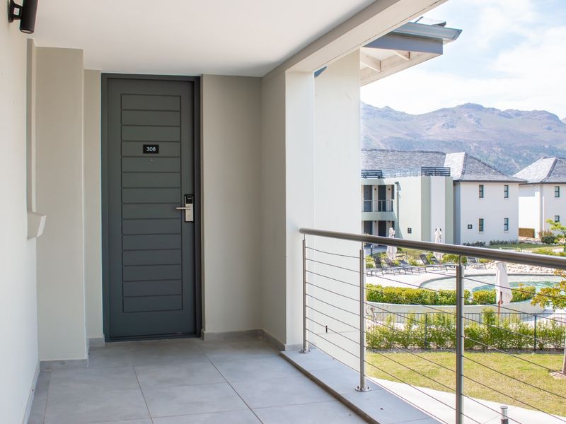 A clean, modern apartment balcony featuring tiled flooring, a secure entrance door, and stainless steel cable railings overlooking the complex pool and mountain views.
