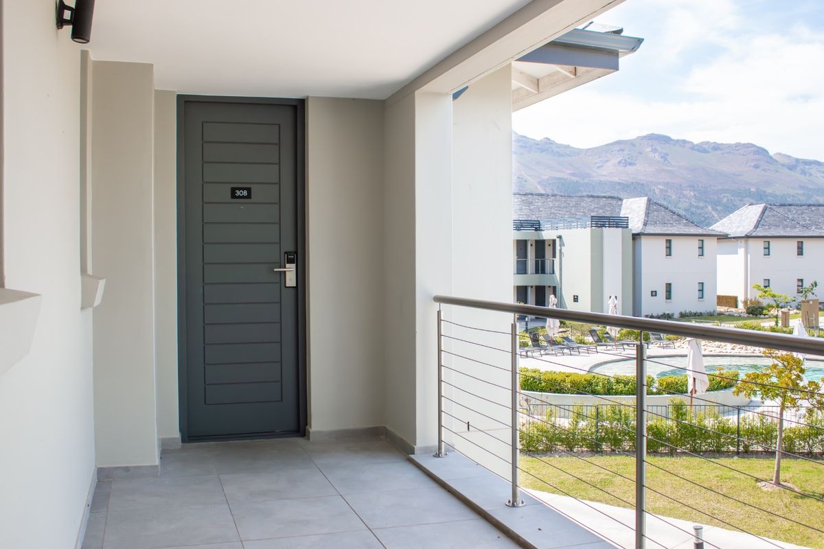 A clean, modern apartment balcony featuring tiled flooring, a secure entrance door, and stainless steel cable railings overlooking the complex pool and mountain views.