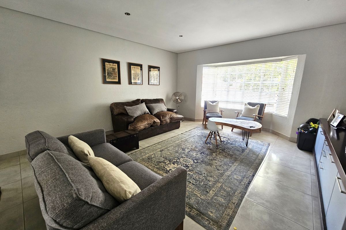 A bright and spacious living room featuring large bay windows with venetian blinds, recessed downlighting, and neutral tiled flooring.