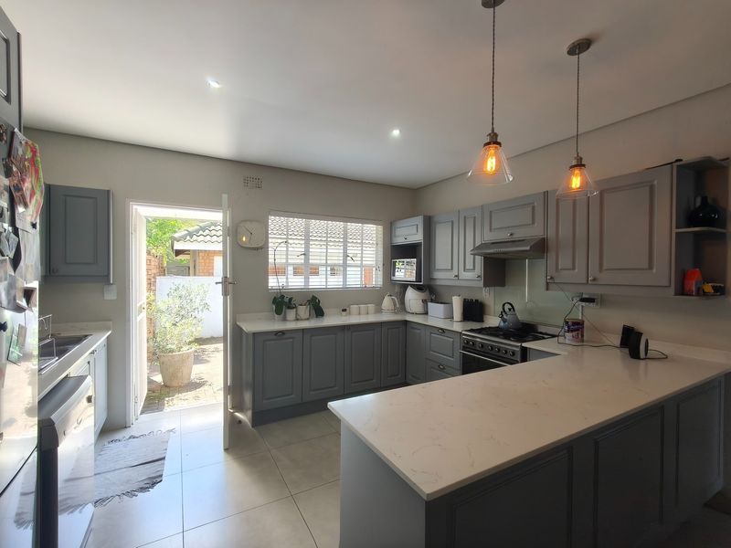 Modern kitchen featuring grey shaker-style cabinetry, quartz countertops, gas hob, and integrated appliances, with direct access to an outdoor patio area.