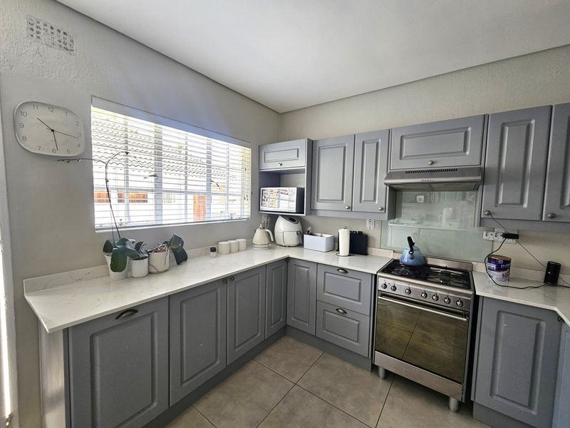 A well-maintained kitchen featuring grey shaker-style cabinetry, stone countertops, a gas stove with an extractor fan, and modern tiled flooring.